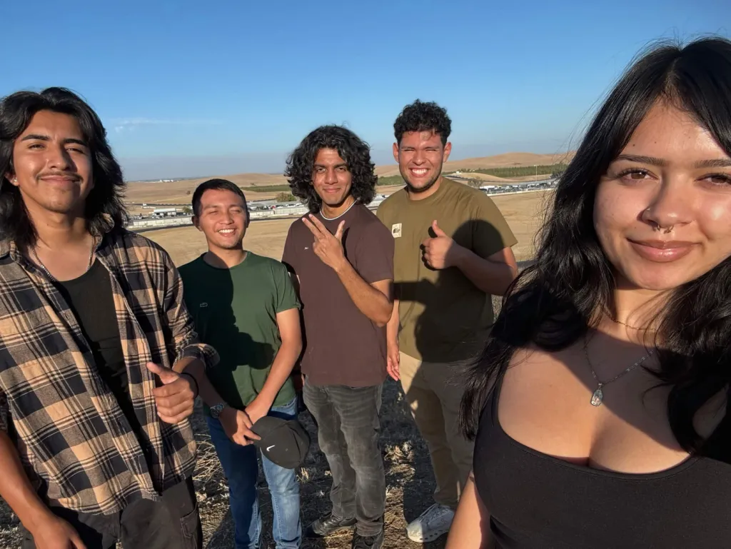 Five Electric Sting Racing team members outdoors beside a racetrack under a blue sky.